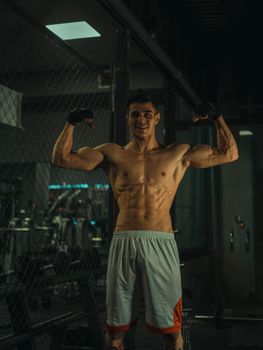 Muscular adult male flexing in the gym with fitness gloves, showcasing strength and fitness.
