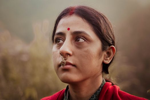Portrait of a woman with a traditional nose ring and red bindi, gazing thoughtfully outdoors.
