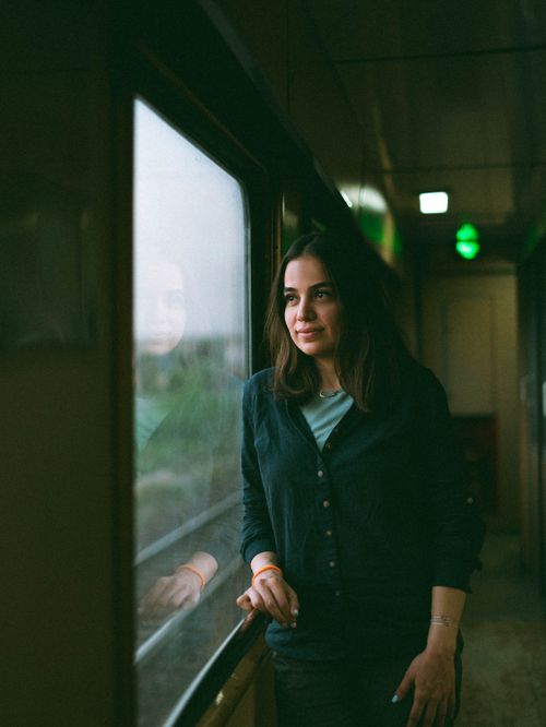 Free A young woman in a train corridor gazes thoughtfully out of the window, capturing a serene moment. Stock Photo