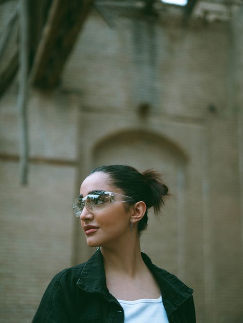 Free Stylish woman with sunglasses posing against a brick wall in an urban setting. Stock Photo