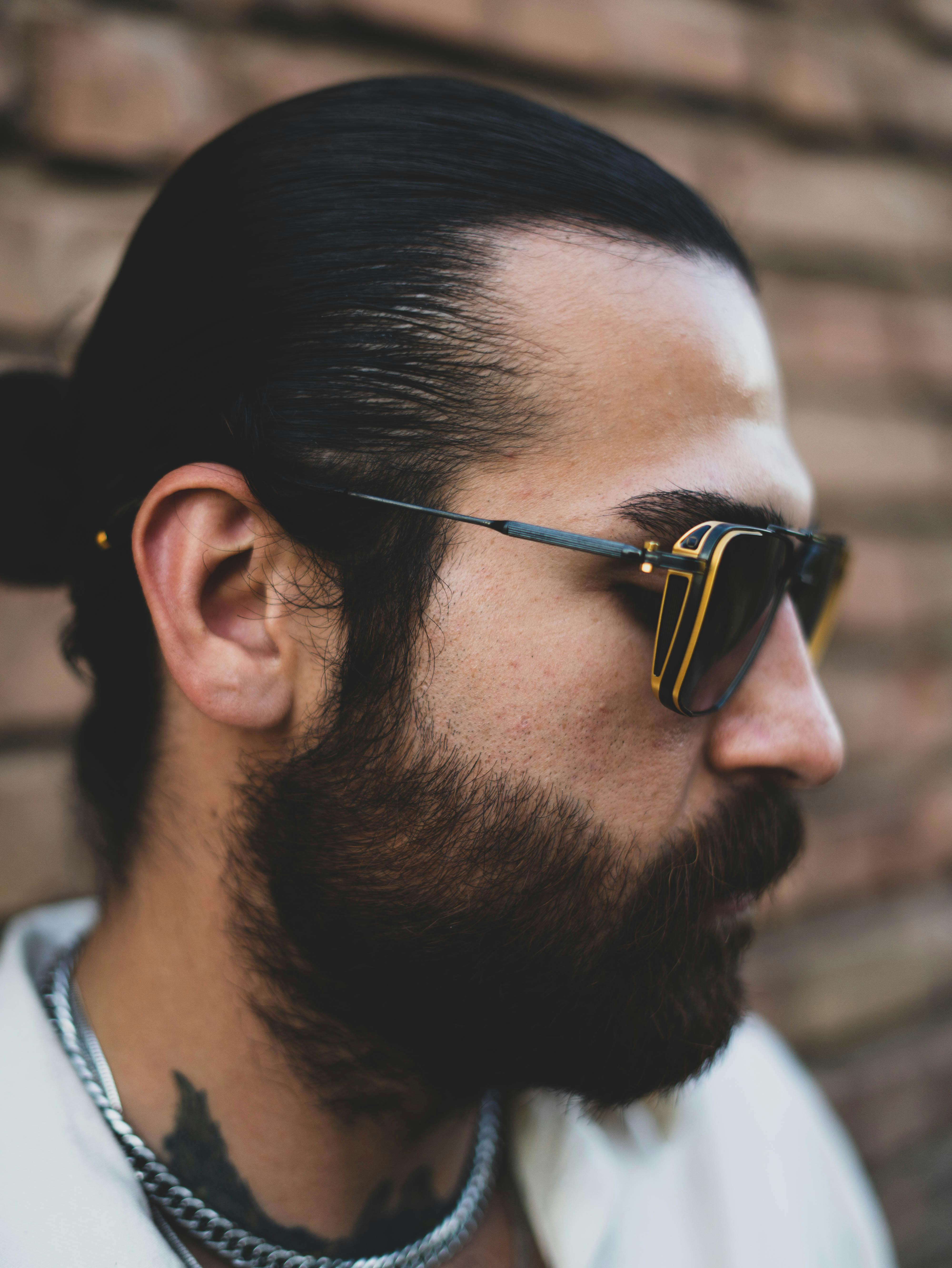 Stylish bearded man wearing sunglasses against a brick wall.