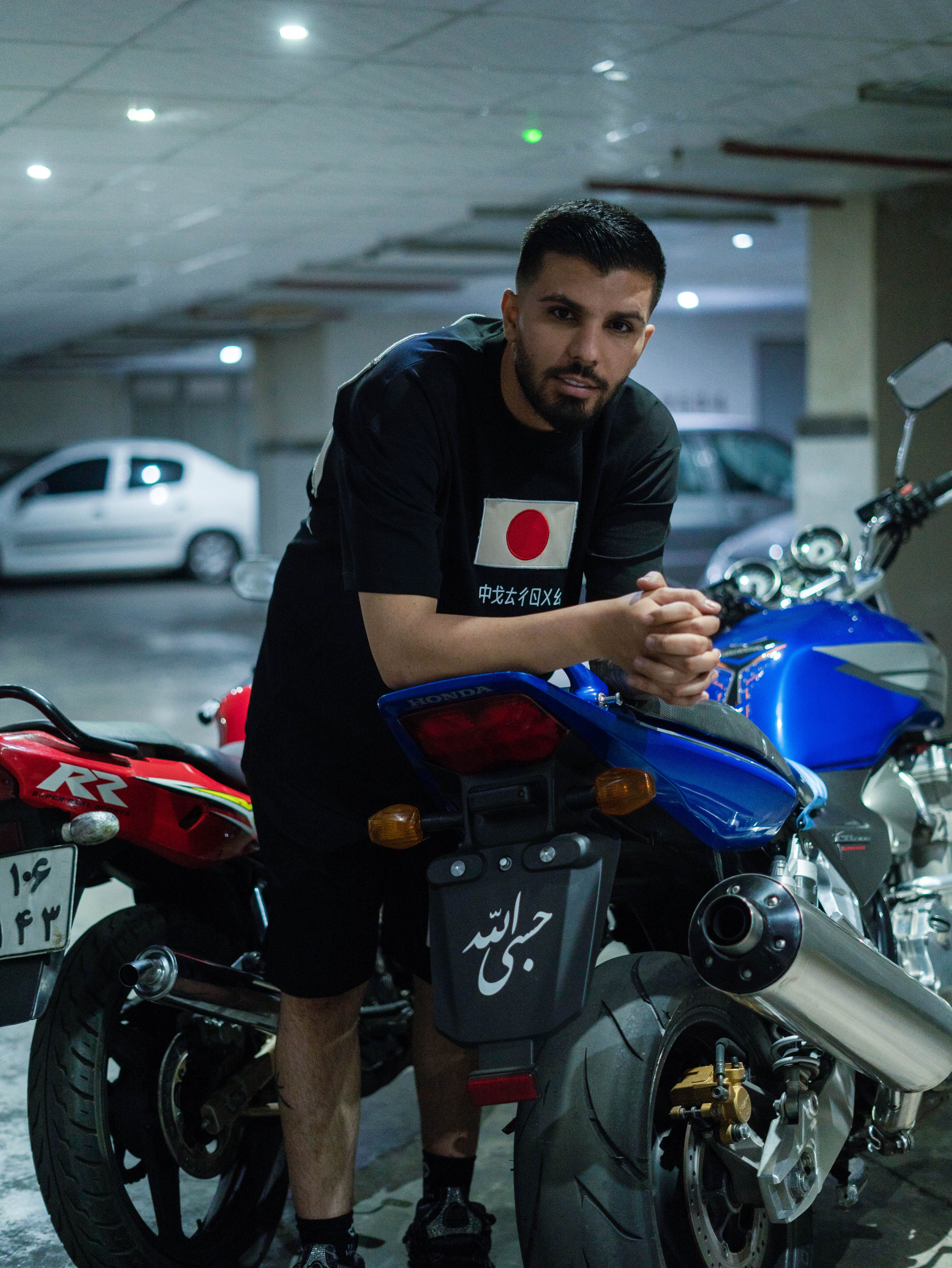 Man leaning on a motorcycle in a dimly lit garage with multiple bikes around.