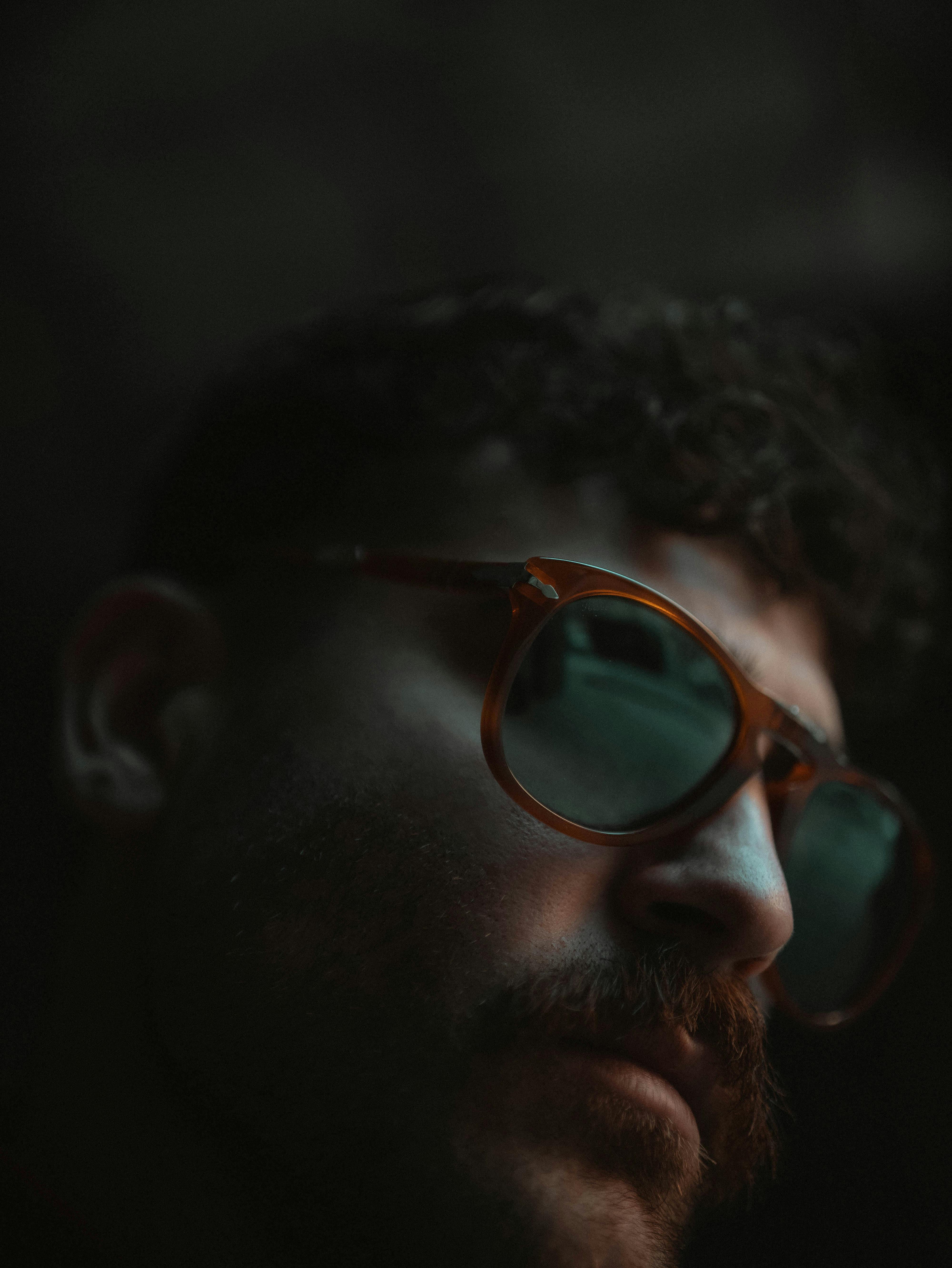 bezplatná Detailní záběr muže ve slunečních brýlích s reflexními čočkami v temné náladové scéně. Základová fotografie