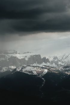 Dramatic scene of storm clouds looming over a snow-covered mountain range.