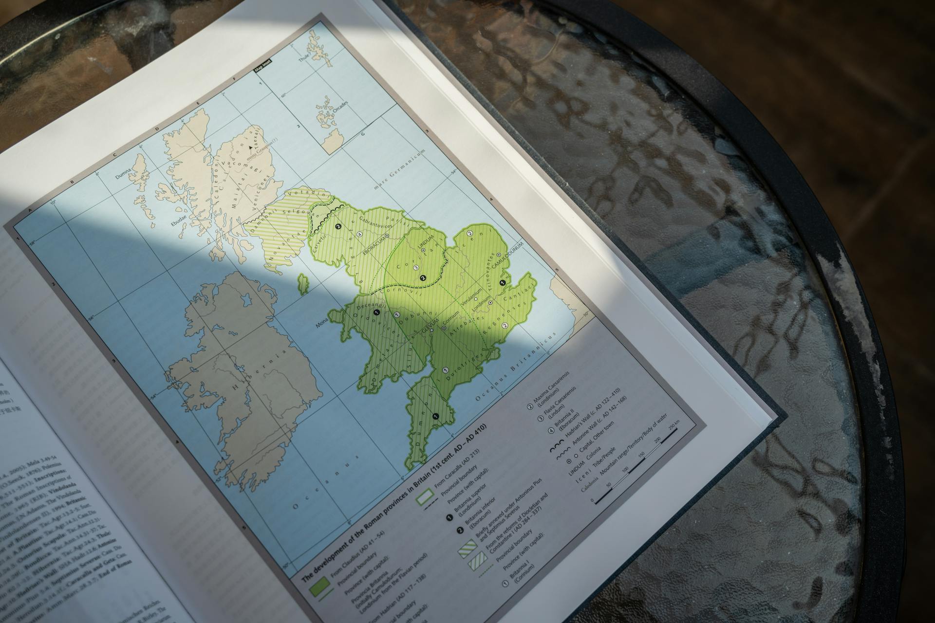 A detailed map of Roman Britain in an open book on a glass table.