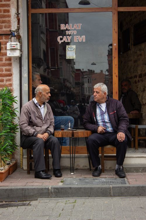 Free Two men chatting at Balat 1979 Çay Evi, a cozy tea house entrance on a bustling street. Stock Photo