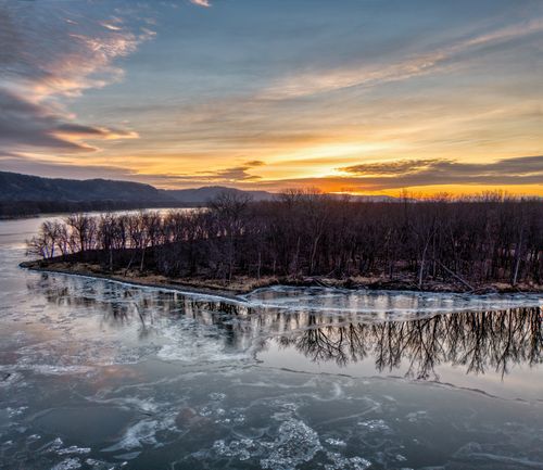 Free A tranquil winter sunrise over a frozen lake with trees reflecting on the icy surface in Minnesota. Stock Photo