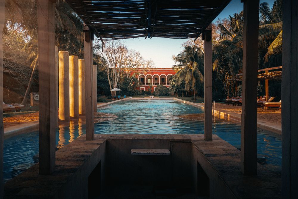 Piscina de una hacienda colonial yucateca con arcos rojos y palmeras al ocaso