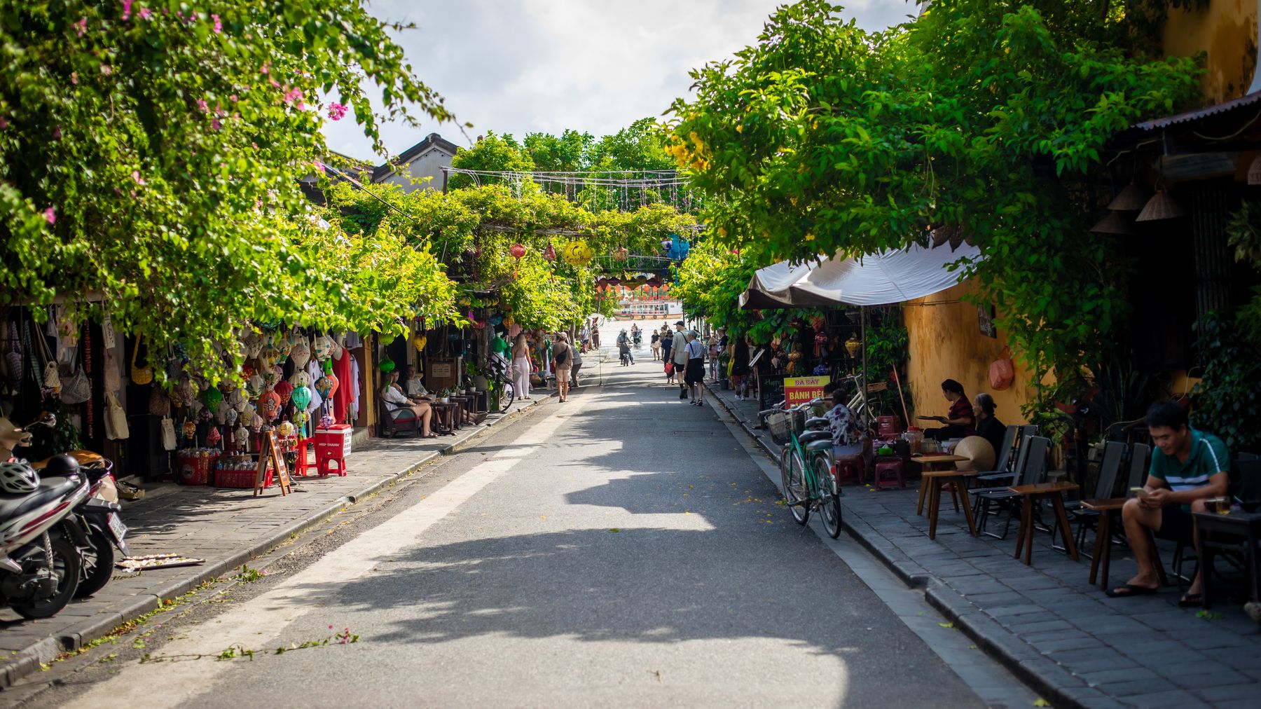 Explore the vibrant street life of Hα»i An with its colorful shops and lush greenery.