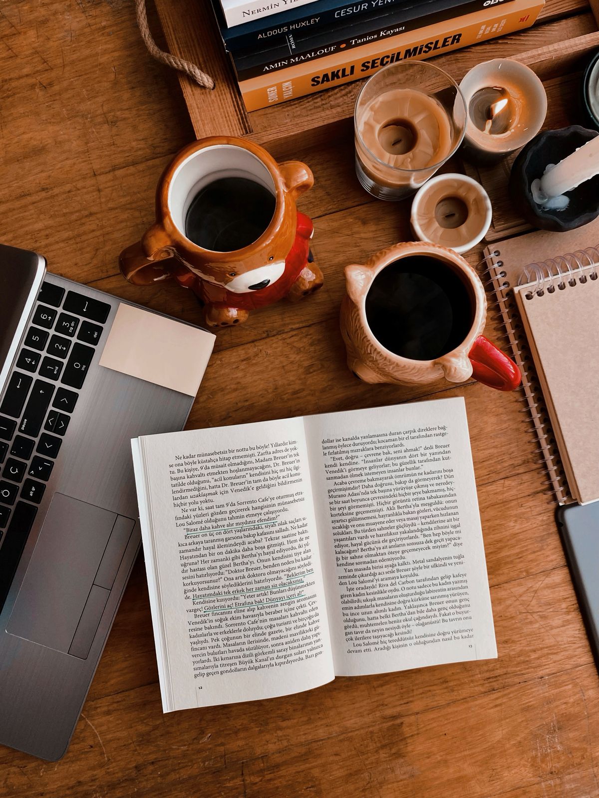 An open book, coffee and laptop on a wooden desk