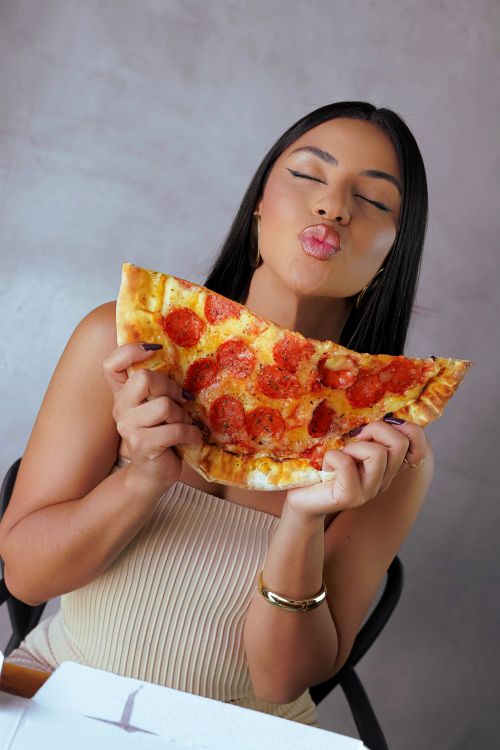 Free Woman expressing happiness while holding a large slice of pepperoni pizza. Indoor setting with a joyful mood. Stock Photo