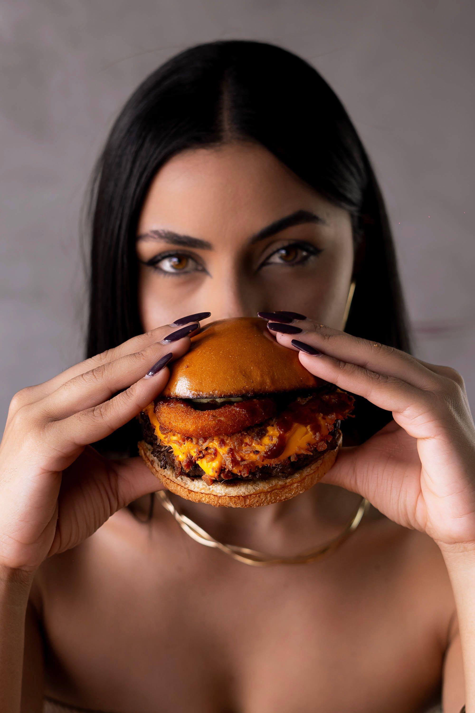 Close-up of a woman holding a delicious gourmet hamburger with a focus on the rich toppings.