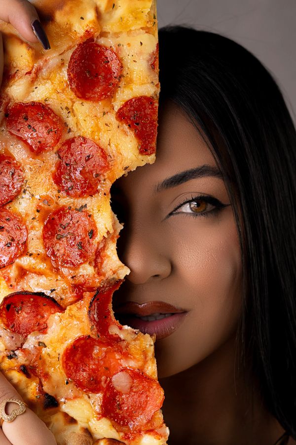 Um retrato impressionante de uma mulher parcialmente escondida por uma fatia de pizza de calabresa com queijo.