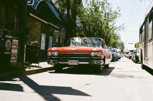 Free Vintage red car parked in city street with bright sunlight and urban background. Stock Photo