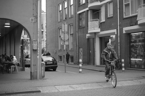 Free Black and white photo of a cyclist riding through an urban street with buildings. Stock Photo