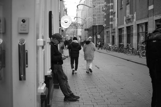 Black and white street view with people walking and an individual leaning against a wall.