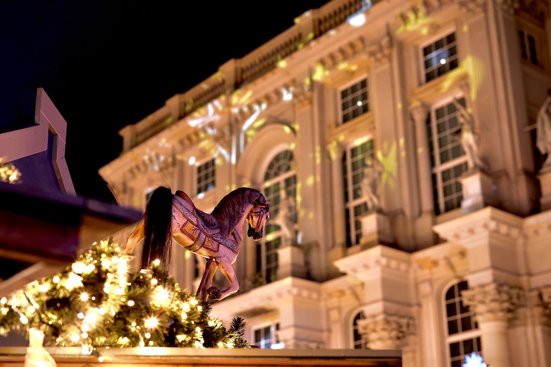 Festive Christmas market scene with illuminated carousel horse and grand building backdrop.