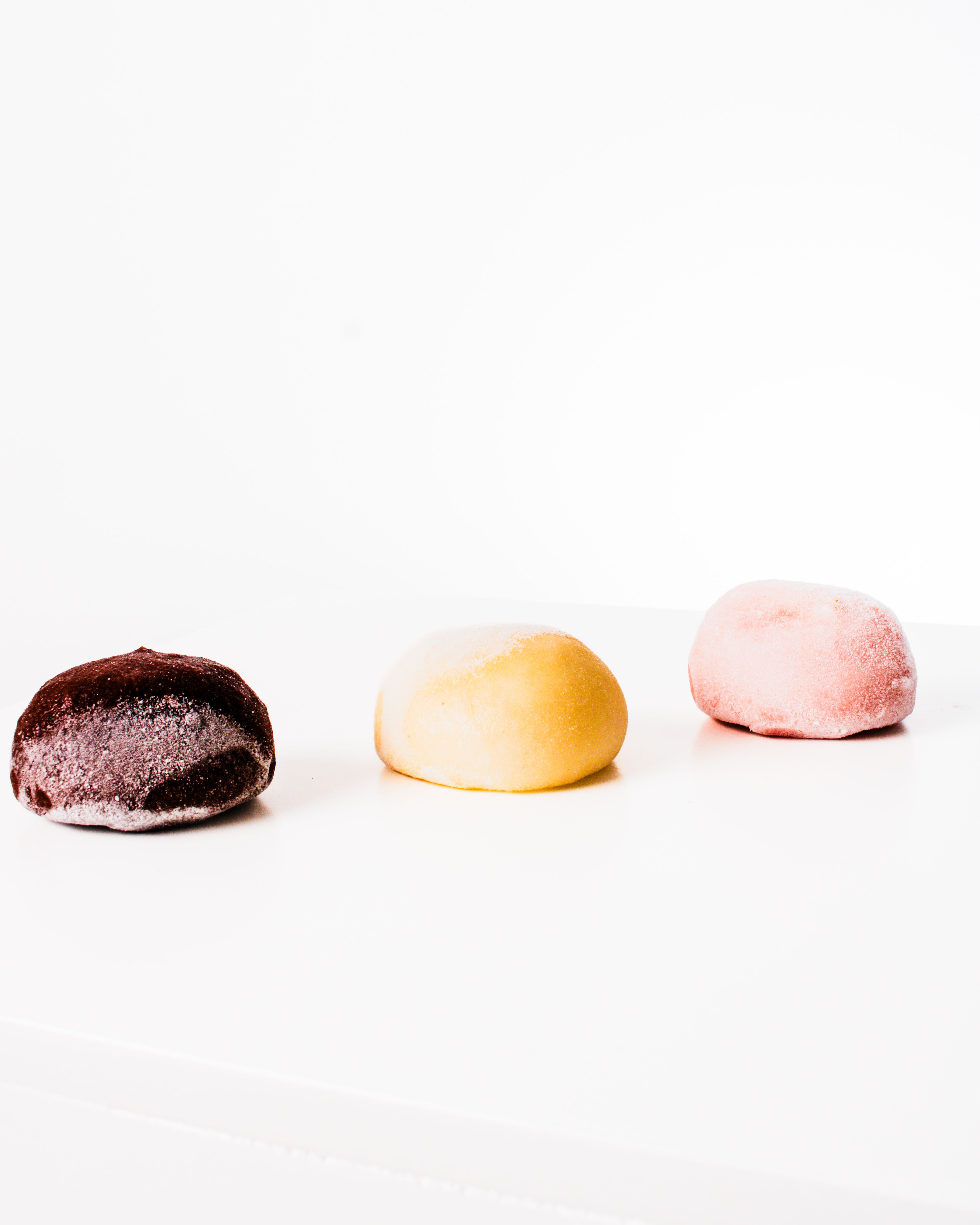 Three colorful mochi desserts arranged on a white surface with a minimalist background.