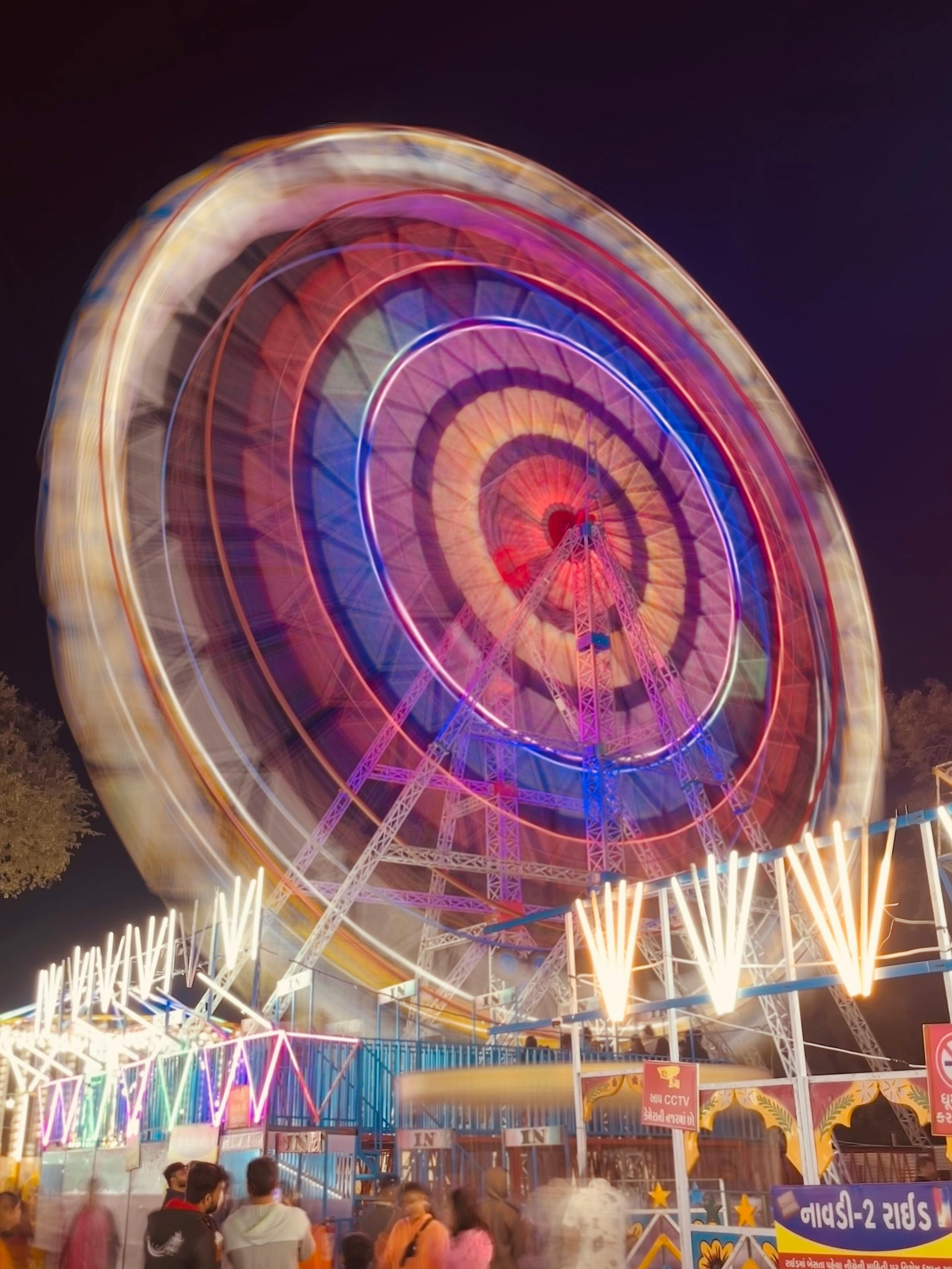 Gratuit Longue exposition dynamique d'une grande roue en rotation lors d'un carnaval nocturne, capturant des lumières et des personnes dynamiques. Photos