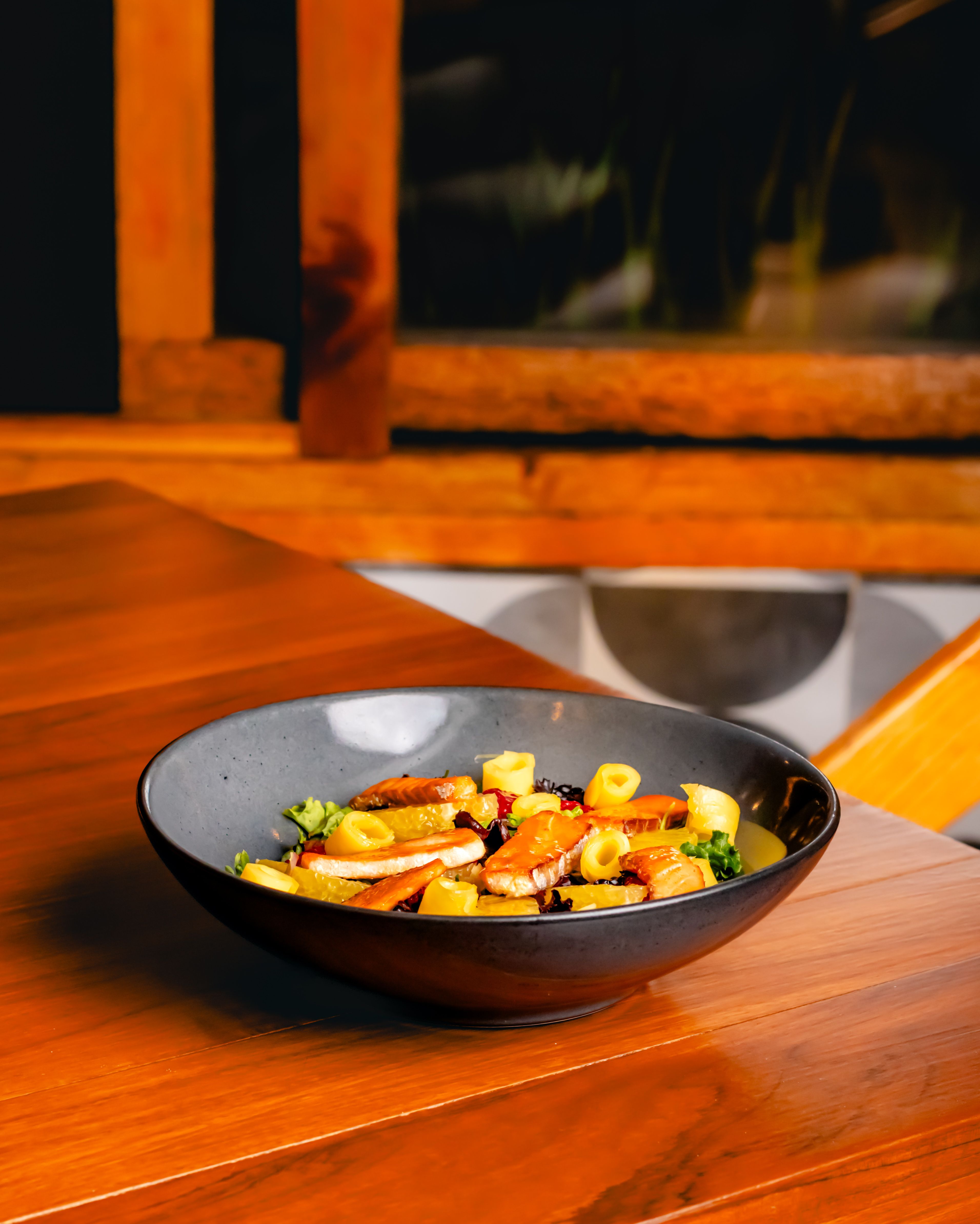 A vibrant vegetable dish elegantly presented in a black bowl on a wooden dining table.
