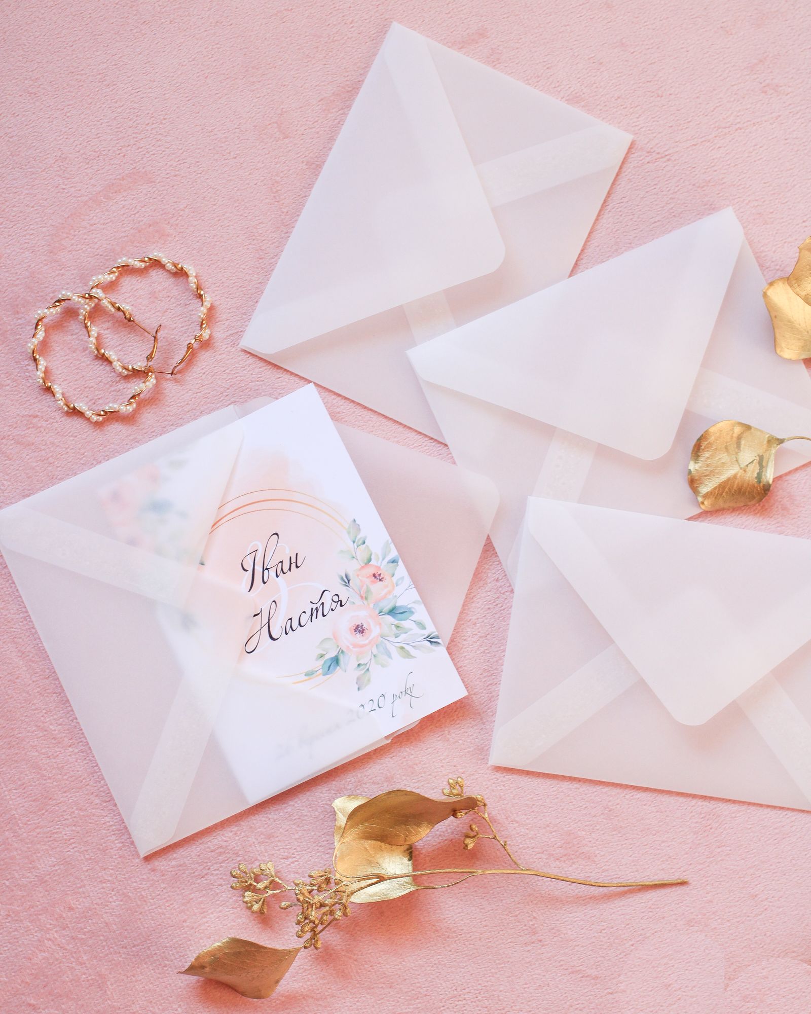 A floral invitation card and envelopes arranged on a soft pink background.