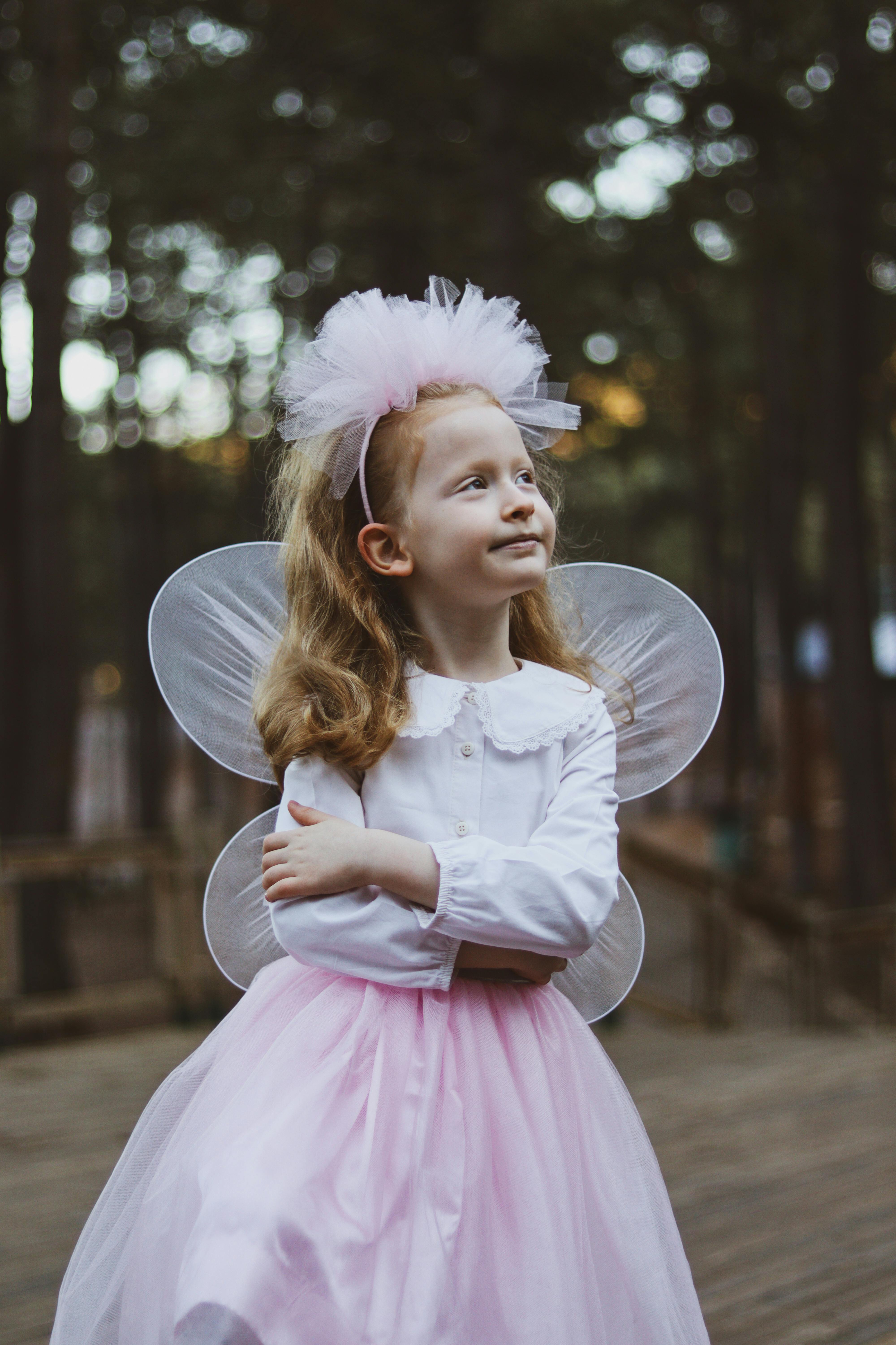 Young girl dressed as a fairy with butterfly wings in a forest setting.