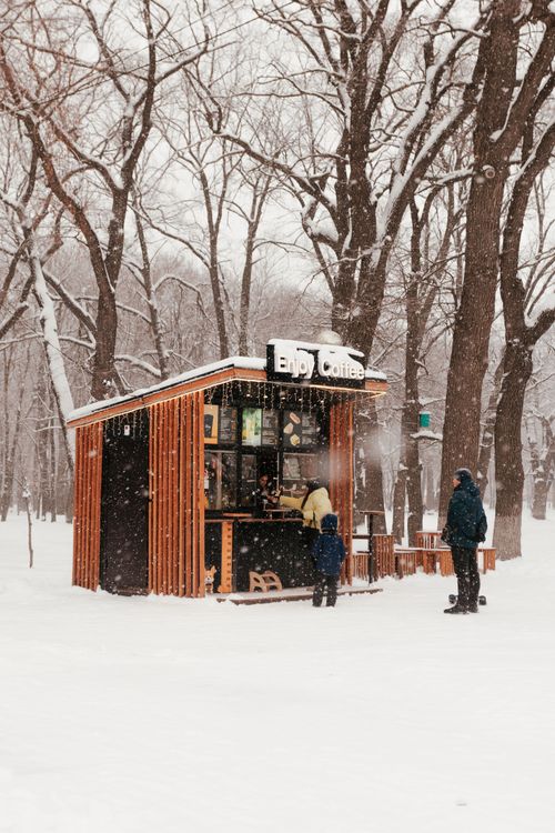Free Snow-covered coffee kiosk in park with people warming up during winter day. Stock Photo