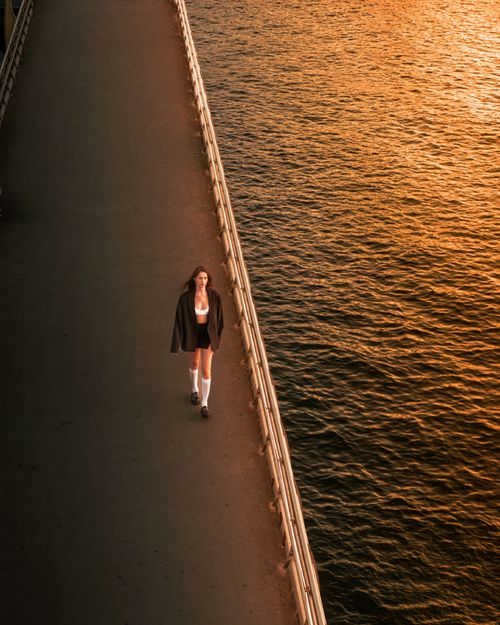 Free A woman walks on a bridge during sunset, with picturesque orange reflections on the water. Stock Photo