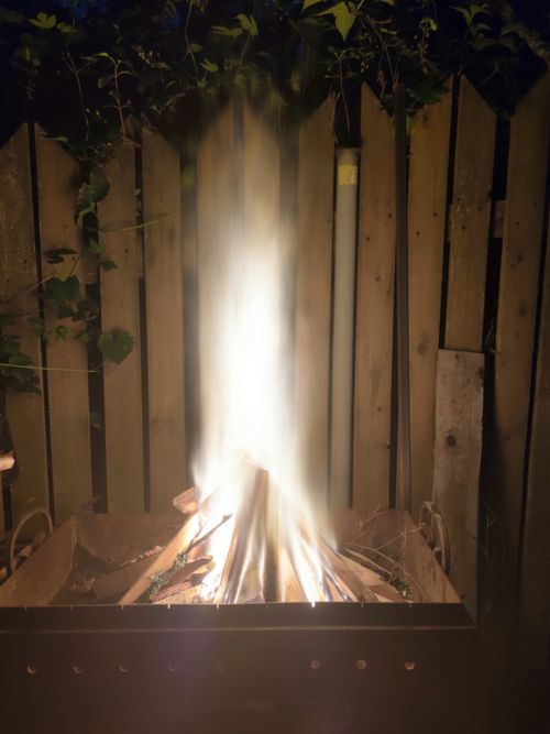 Free A bright bonfire illuminating a dark outdoor setting with a wooden fence backdrop. Stock Photo