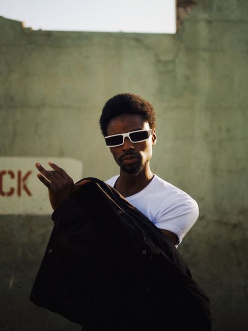 Confident man with sunglasses poses outdoors in Kaduna, Nigeria, showcasing urban style.