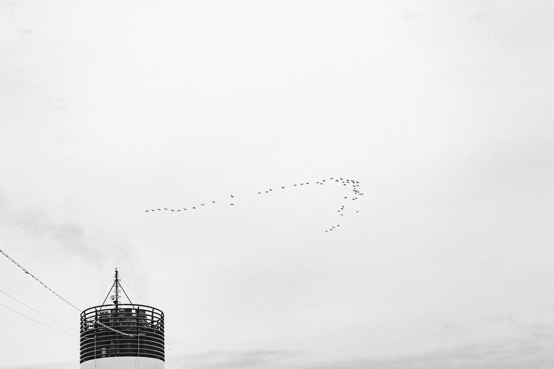 A minimalist black and white image showcasing a ship funnel with birds flying in a cloudy sky.