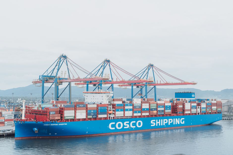 Photo by SAULO LEITE A large cargo ship named COSCO Shipping Argentina docked at a sea port with cranes and container stacks.