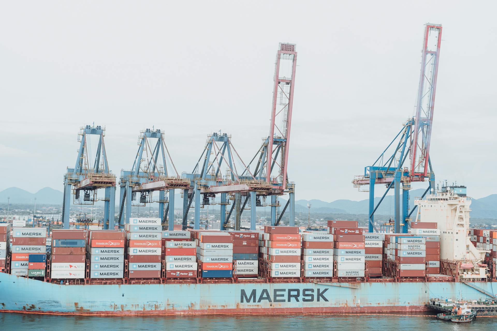 Container ship Maersk loading at a busy industrial port under cranes.