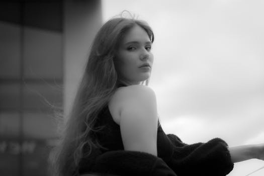 A black and white portrait of a woman outdoors with a contemplative expression in an urban setting.