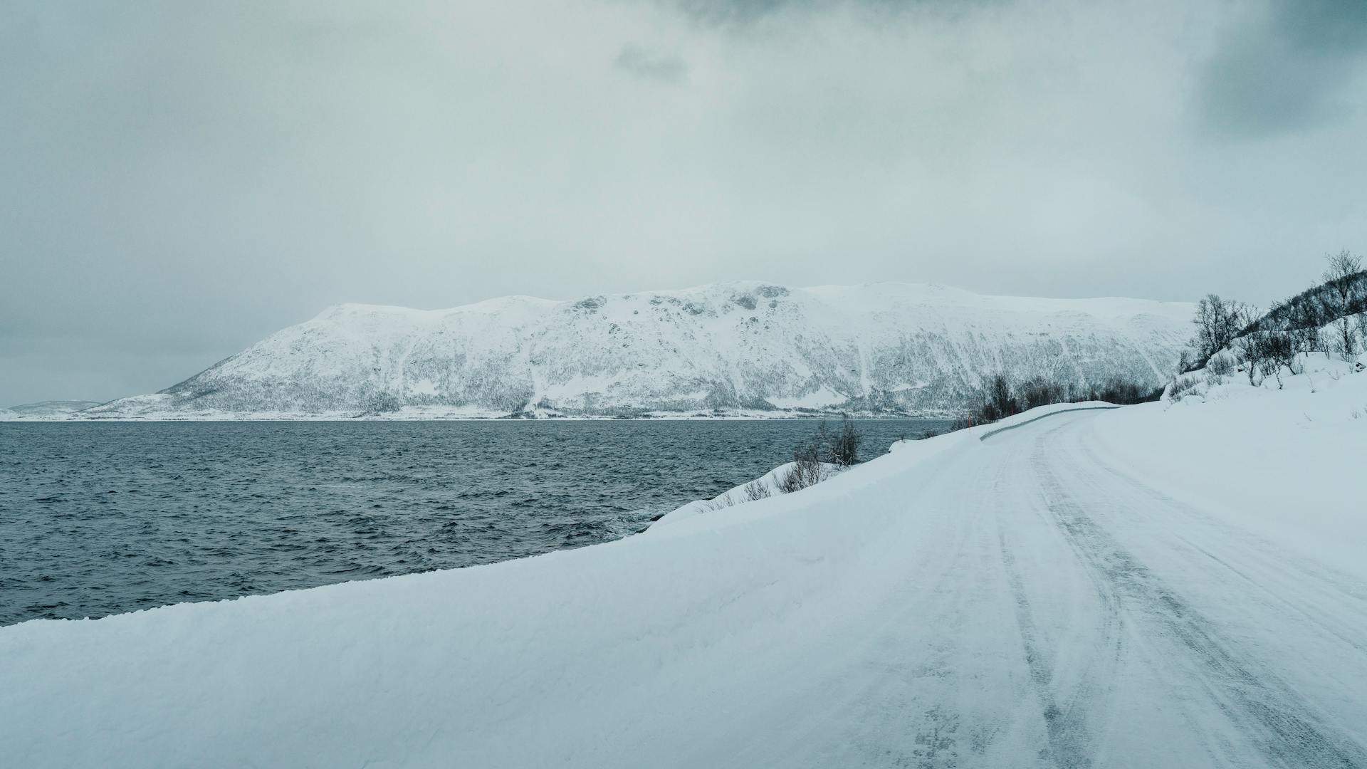 A scenic winter view of a snowy road and frozen coast in Norway.