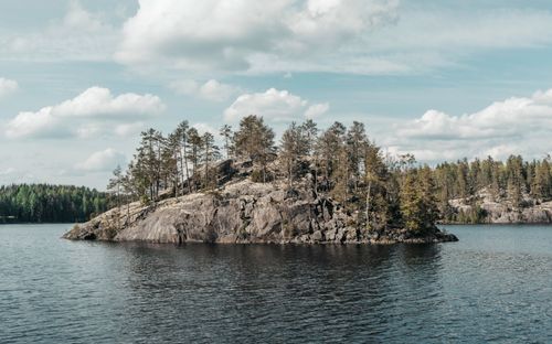 Free A peaceful island with pine trees reflected on a calm Finnish lake under a cloudy sky. Stock Photo