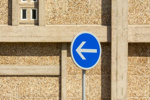 Free A blue traffic sign indicating a mandatory left turn in front of a textured urban wall. Stock Photo