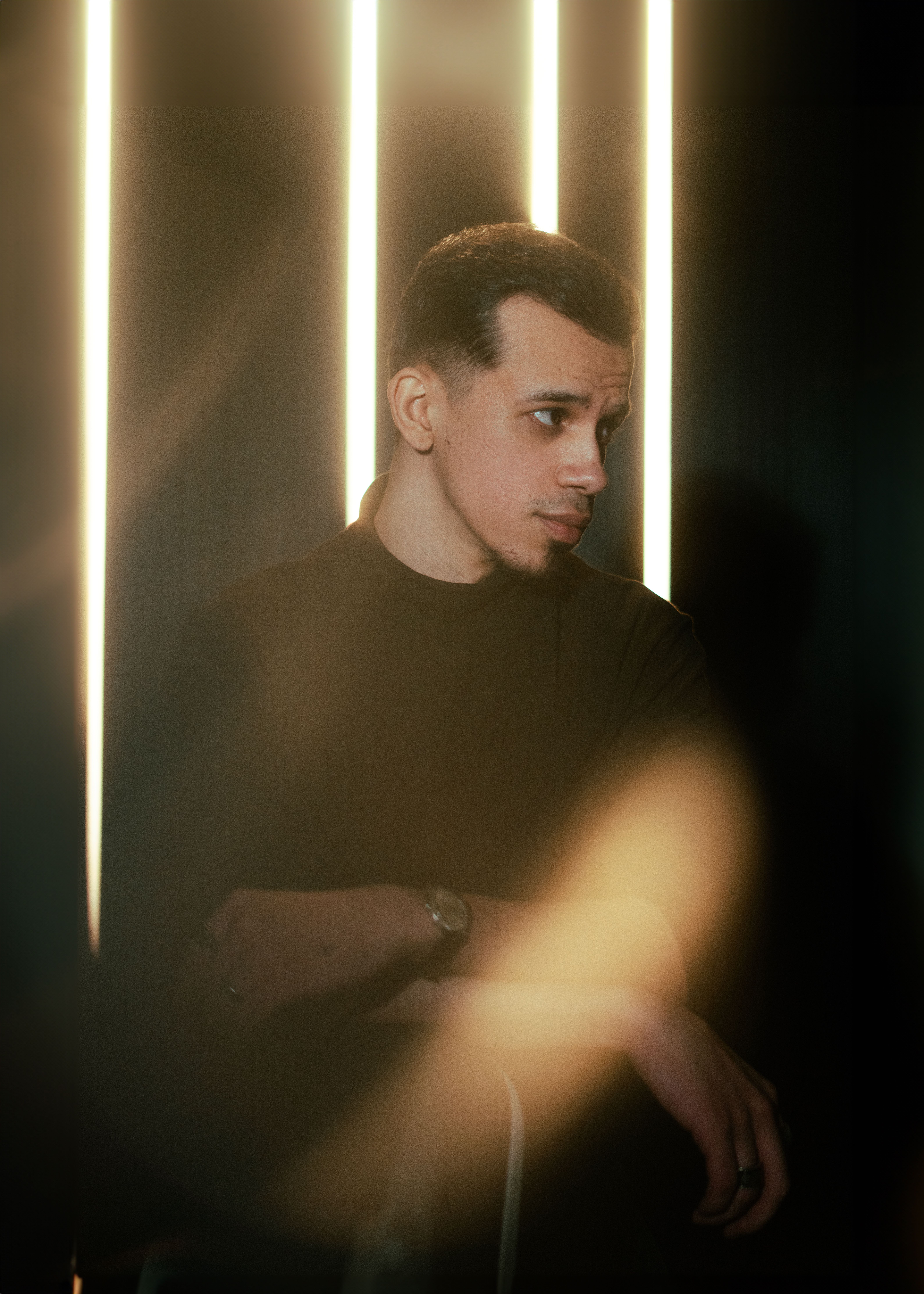 Contemplative young man poses in a dark room with neon lights adding a dramatic effect.
