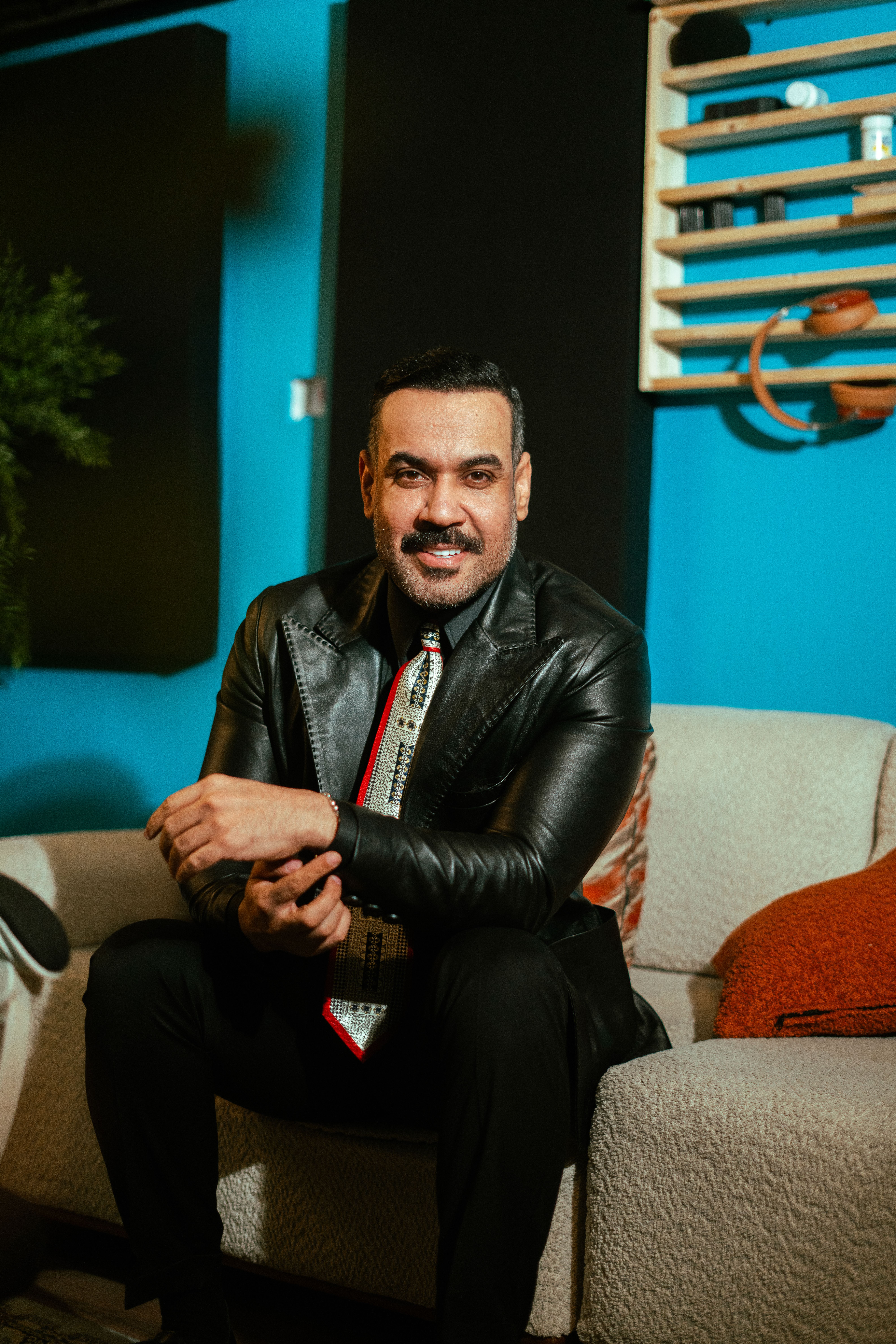 Middle Eastern man in leather jacket sitting confidently in stylish indoor setting.