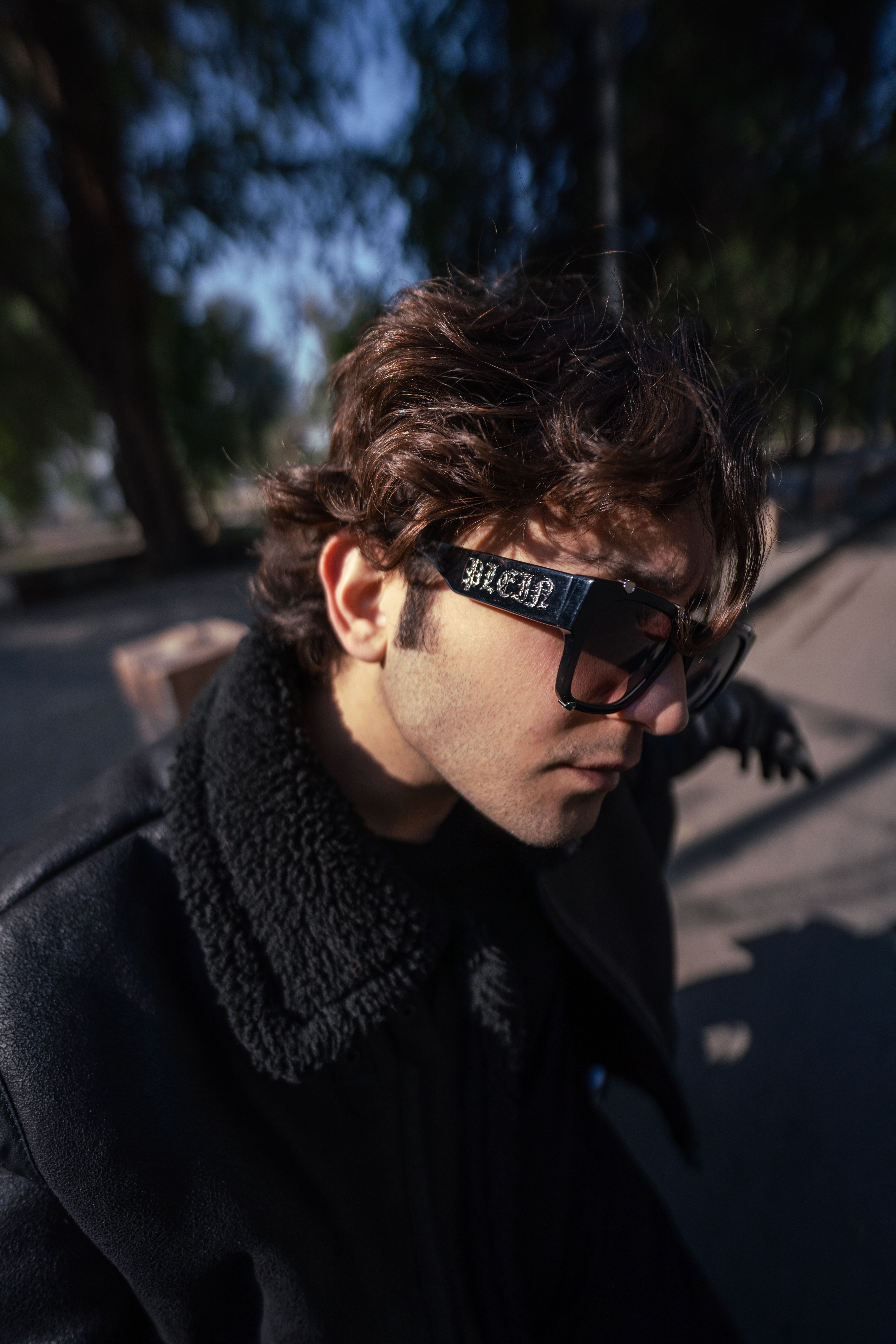 A stylish man with sunglasses walks in a park in Baghdad, Iraq, embracing urban fashion.