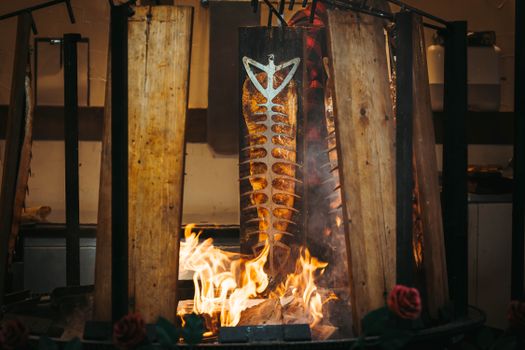 Traditional fish grilling setup with skewered salmon over open fire, evoking a rustic cooking style.