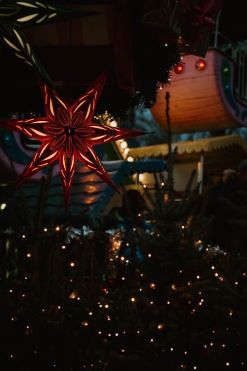 Free Illuminated star lantern hanging in a vibrant Christmas night market setting. Stock Photo