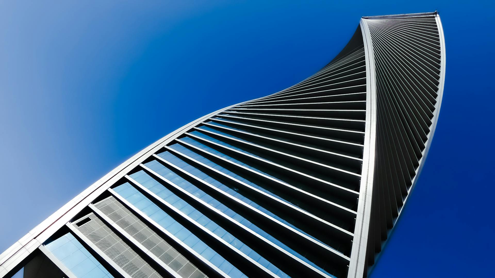 A modern, twisting skyscraper facade against a clear blue sky in Saudi Arabia.