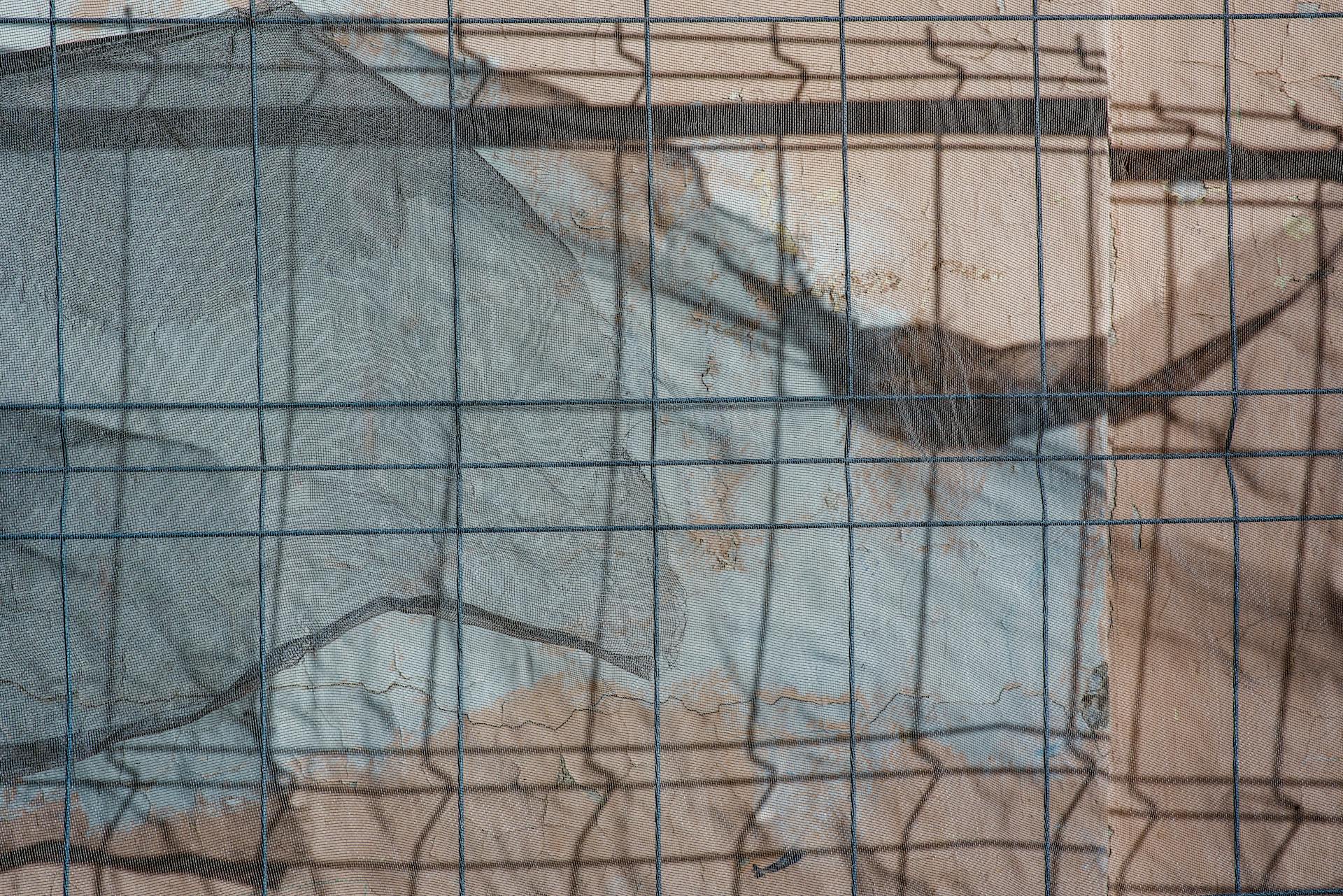 Intriguing abstract view of a wire mesh with shadow and texture overlay, creating a unique pattern.