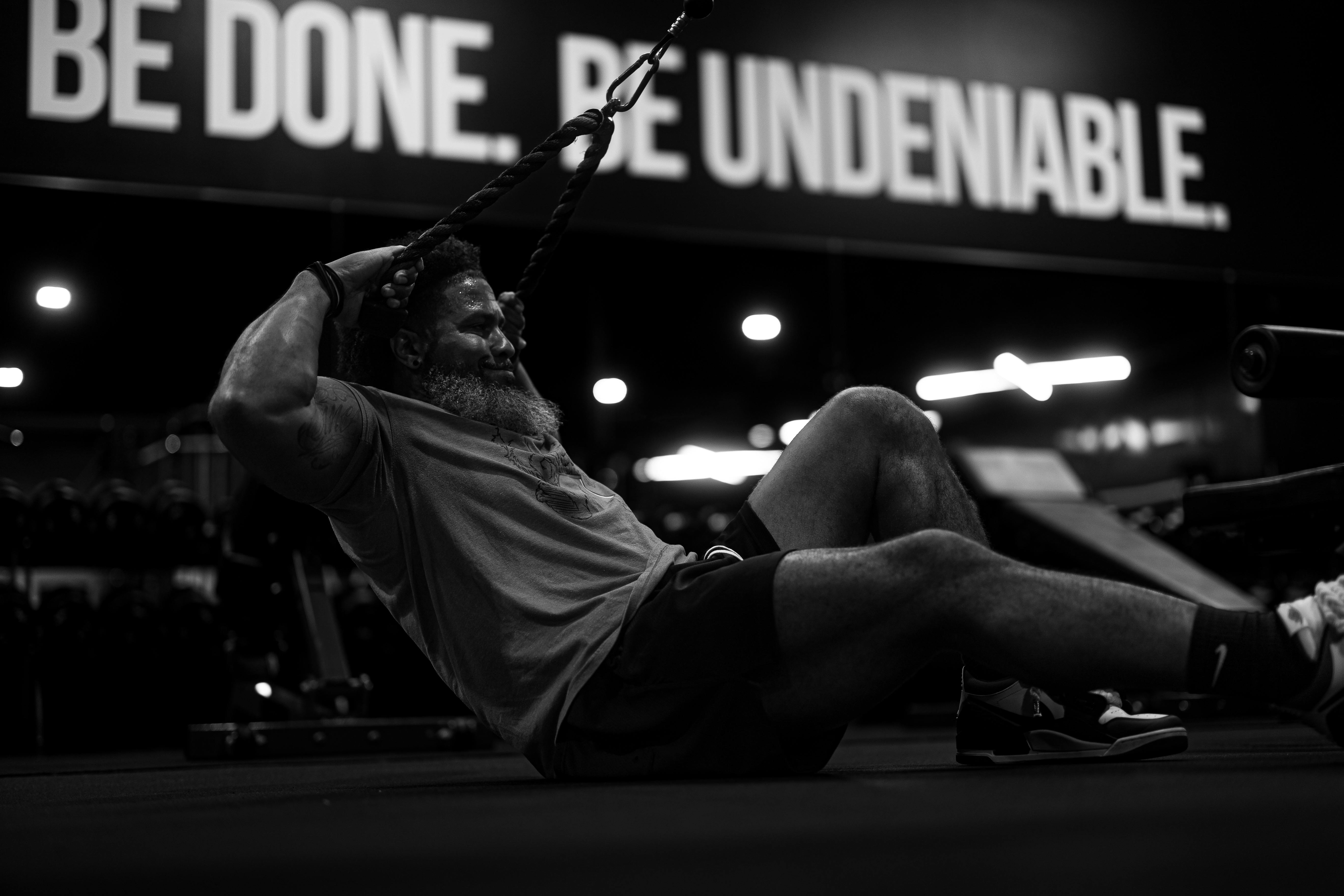 Black and white photo of a man doing intense rope exercises in a gym, embodying determination.