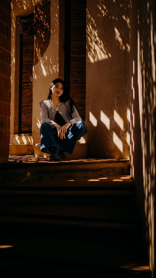 Free A woman poses on a shadowy stairwell with sunlight filtering through, creating a dramatic effect. Stock Photo