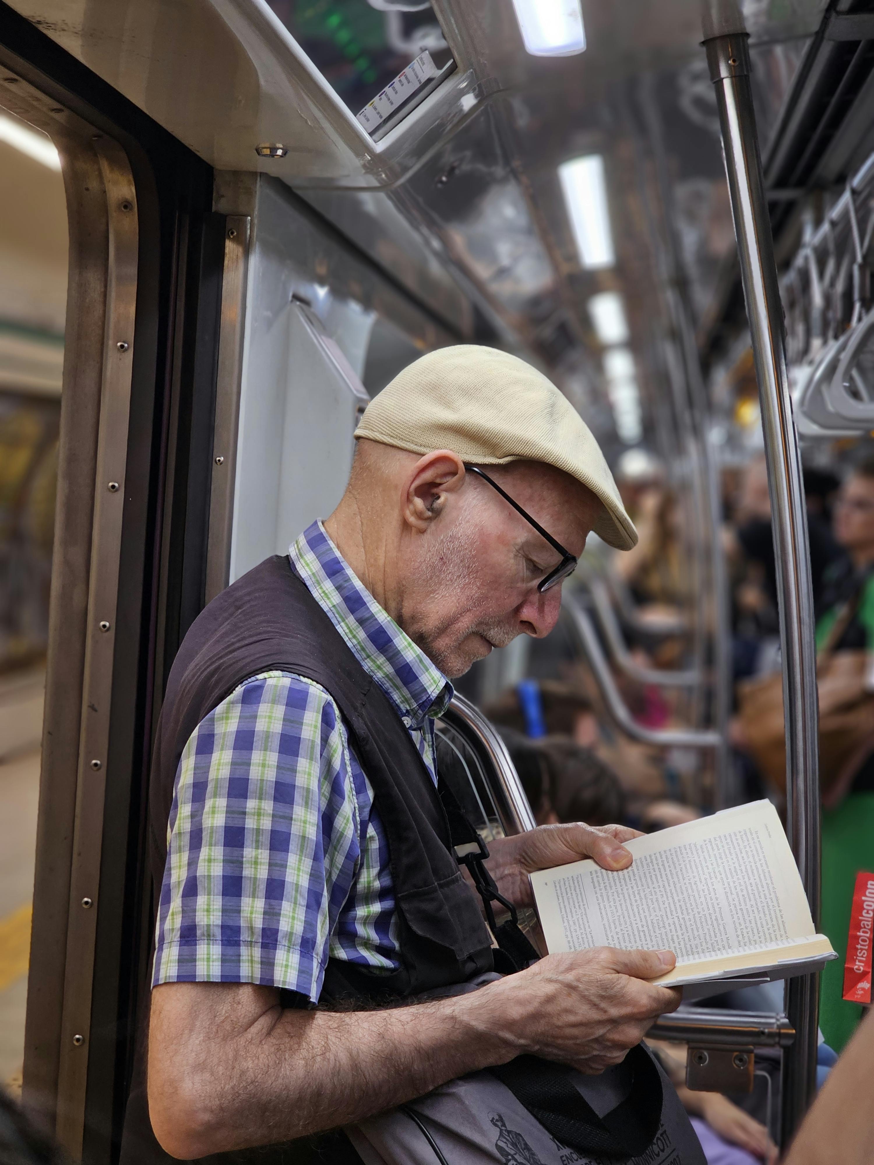 elderly man reading book on busy train