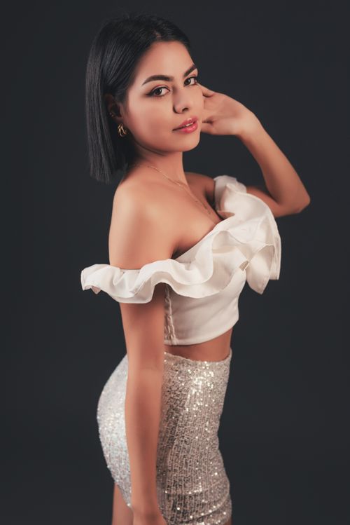 Free Stylish woman posing in white off-shoulder top and sequined skirt in studio. Stock Photo