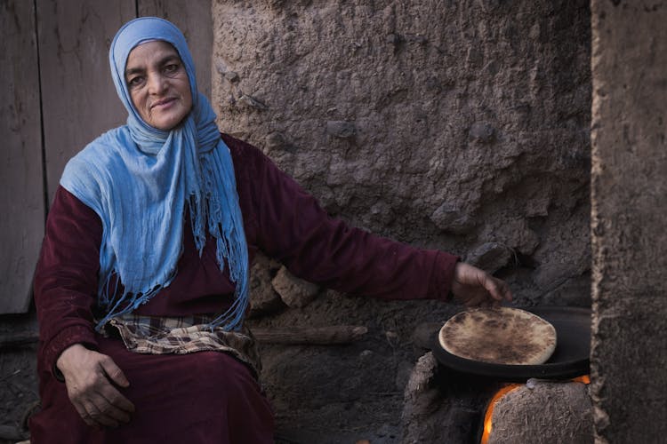 Elderly Woman In A Headscarf Baking A Traditional Bread On A Pan Outdoors 