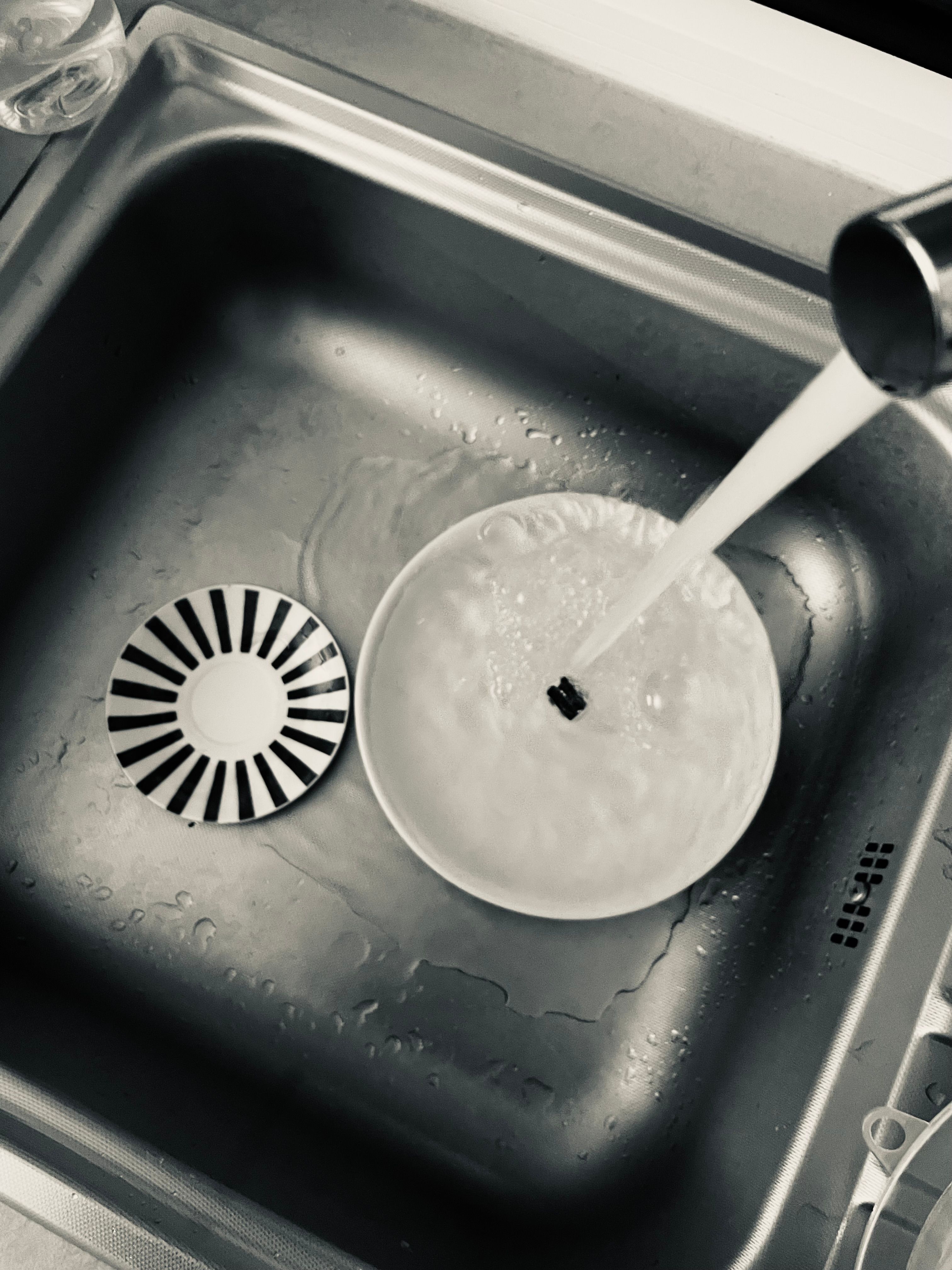 Monochrome view of kitchen sink with dishes being washed under running water